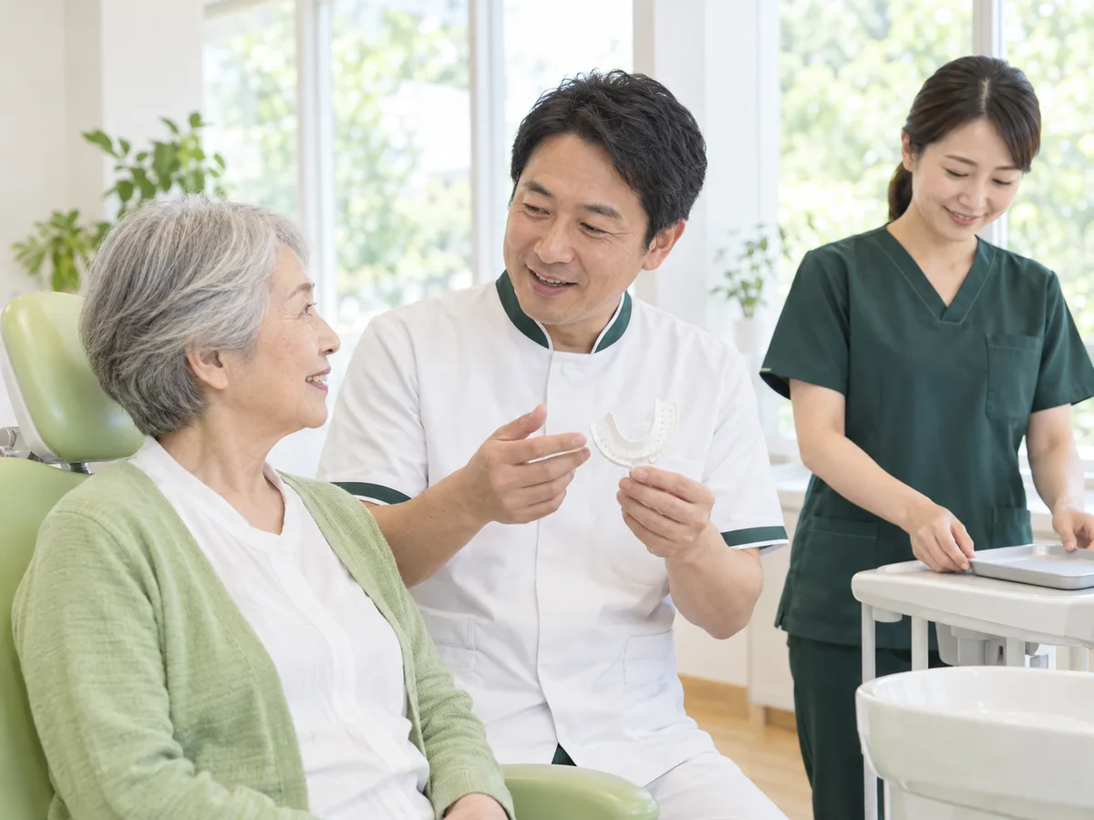 診療台のそばで、歯科医師が白い型取りのトレーを手に持ち、70代の女性に次の手順を説明している