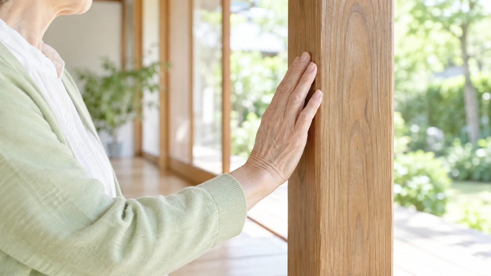 古い木の柱に、支えるように手を添えている70代の女性の手元