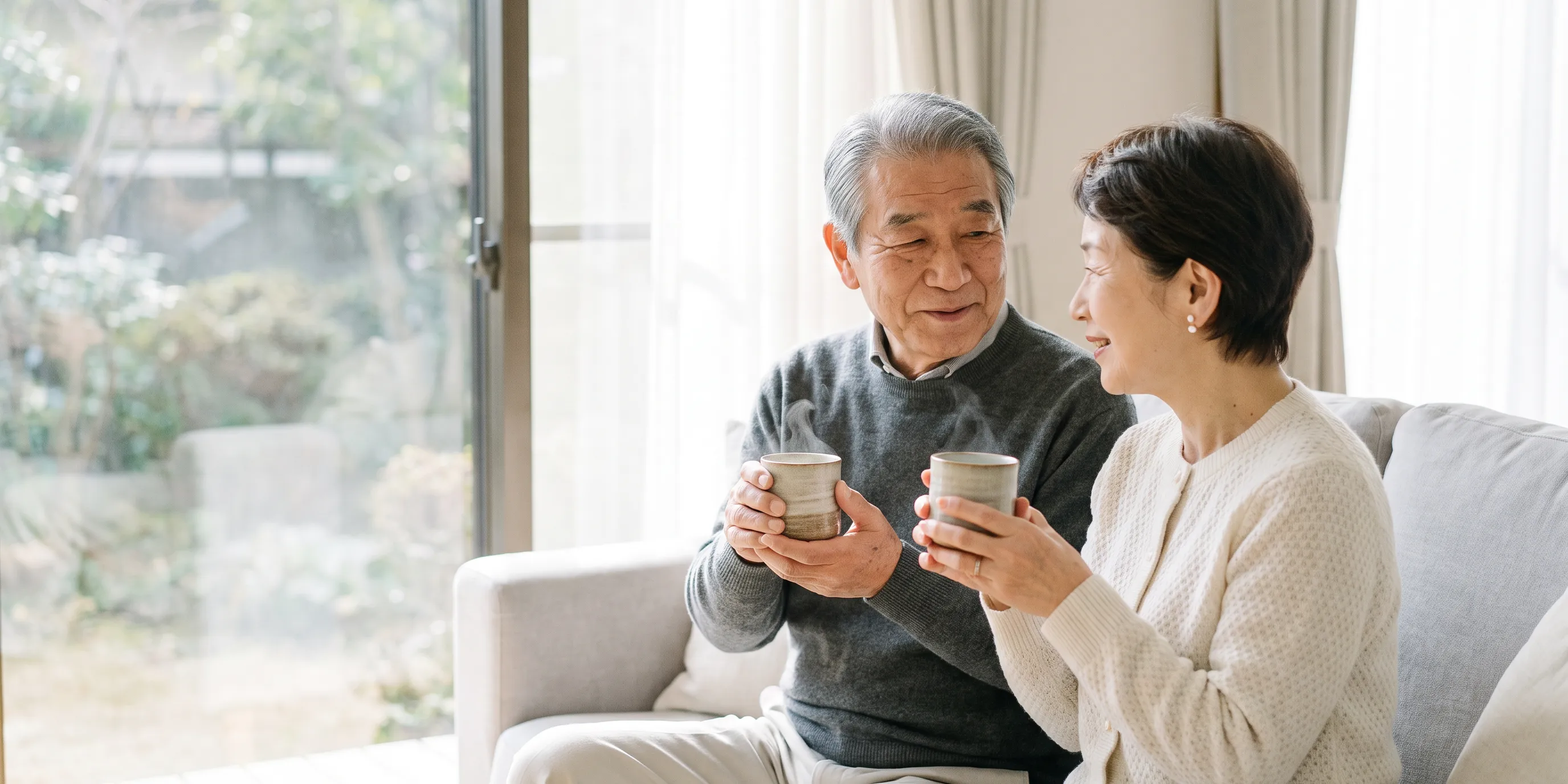 冬の窓辺で、湯のみを手に微笑み合う夫婦
