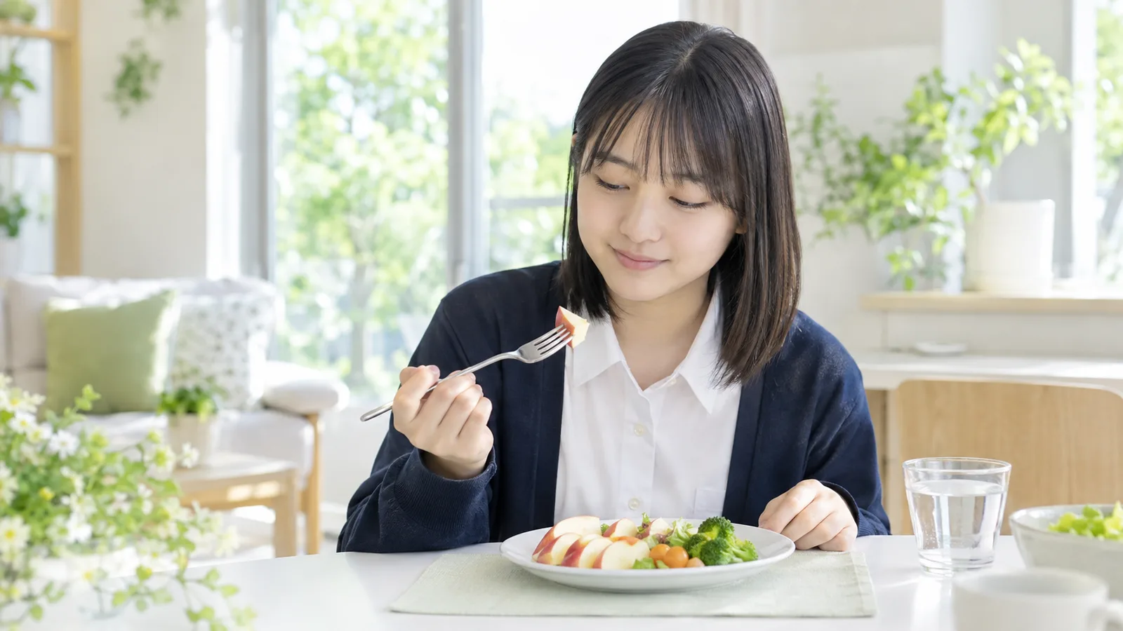 食卓で、りんごを小さく切った皿を前にした高校生の女の子
