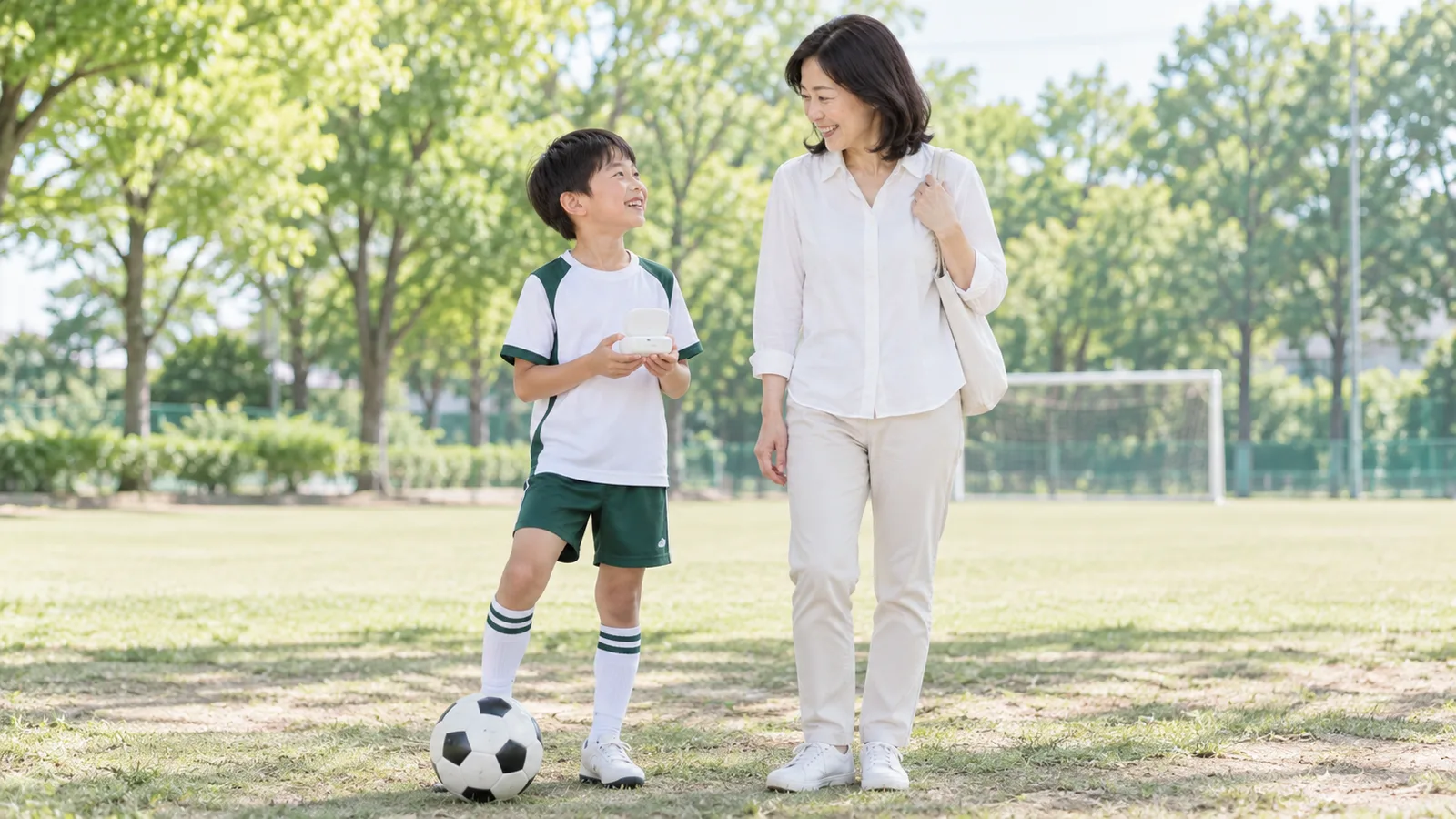 公園で、サッカーの練習着の男の子が母親とマウスガードのケースを手にしている