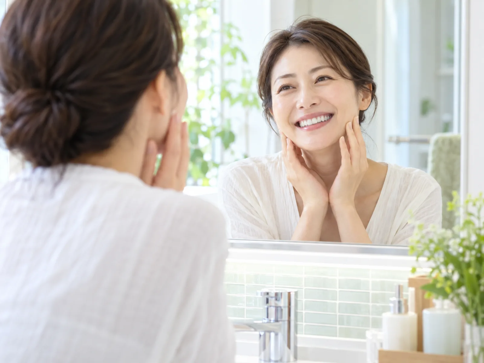 明るい洗面所で、40代の女性が鏡に映った自分の歯並びを見てうれしそうに笑っている