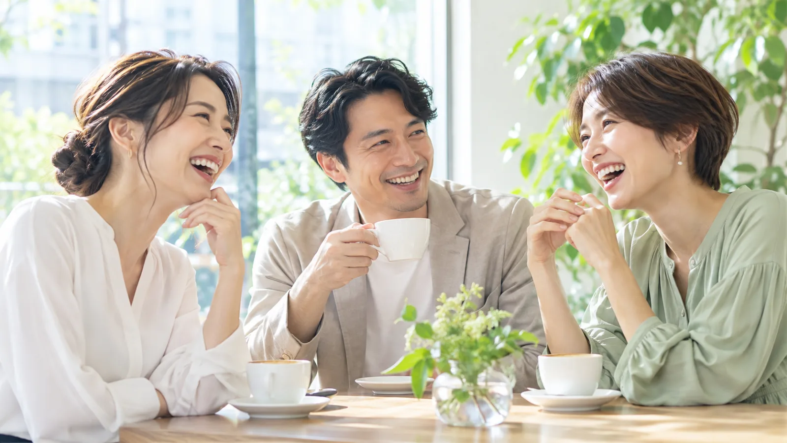 明るいカフェで、30〜40代の友人3人が笑い合っている