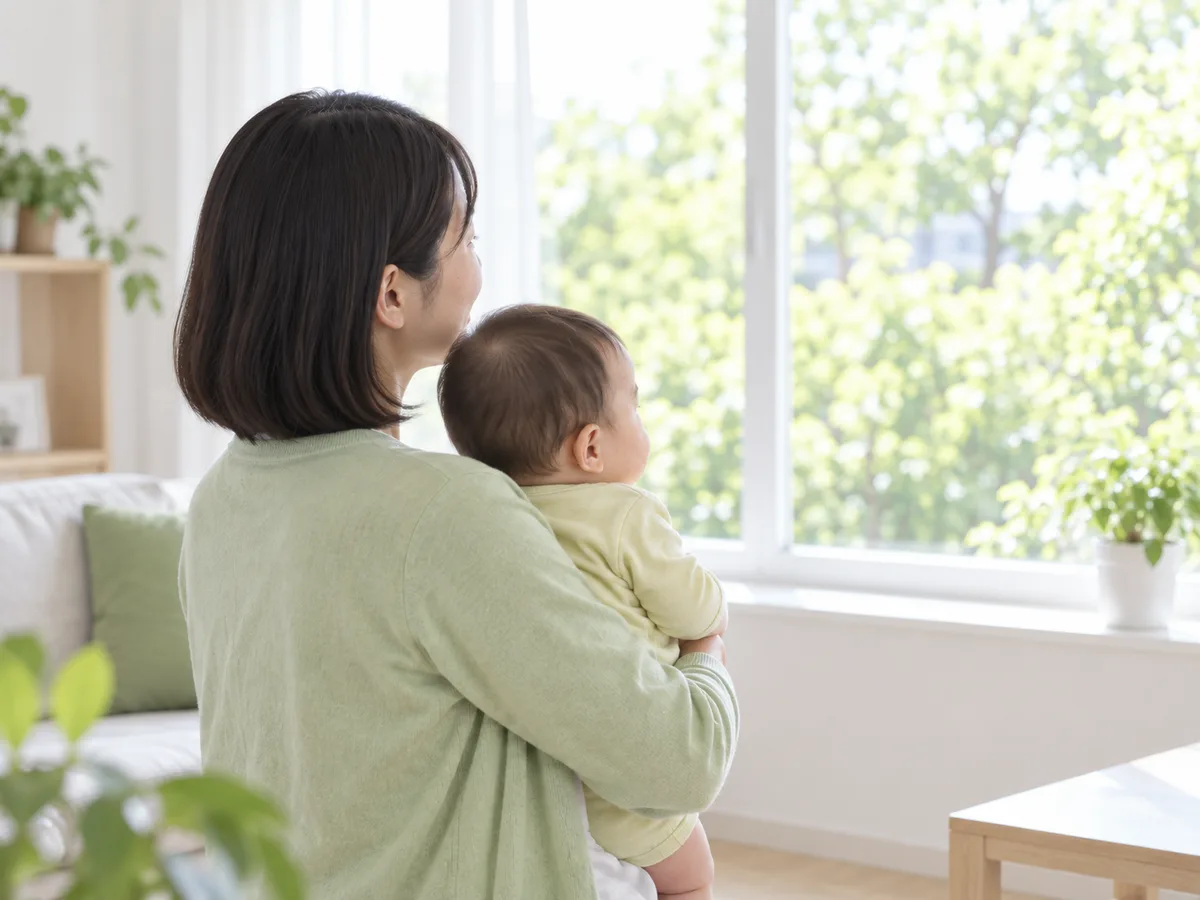 午後の光の中で、赤ちゃんを抱いた母親が窓の外を見ている後ろ姿