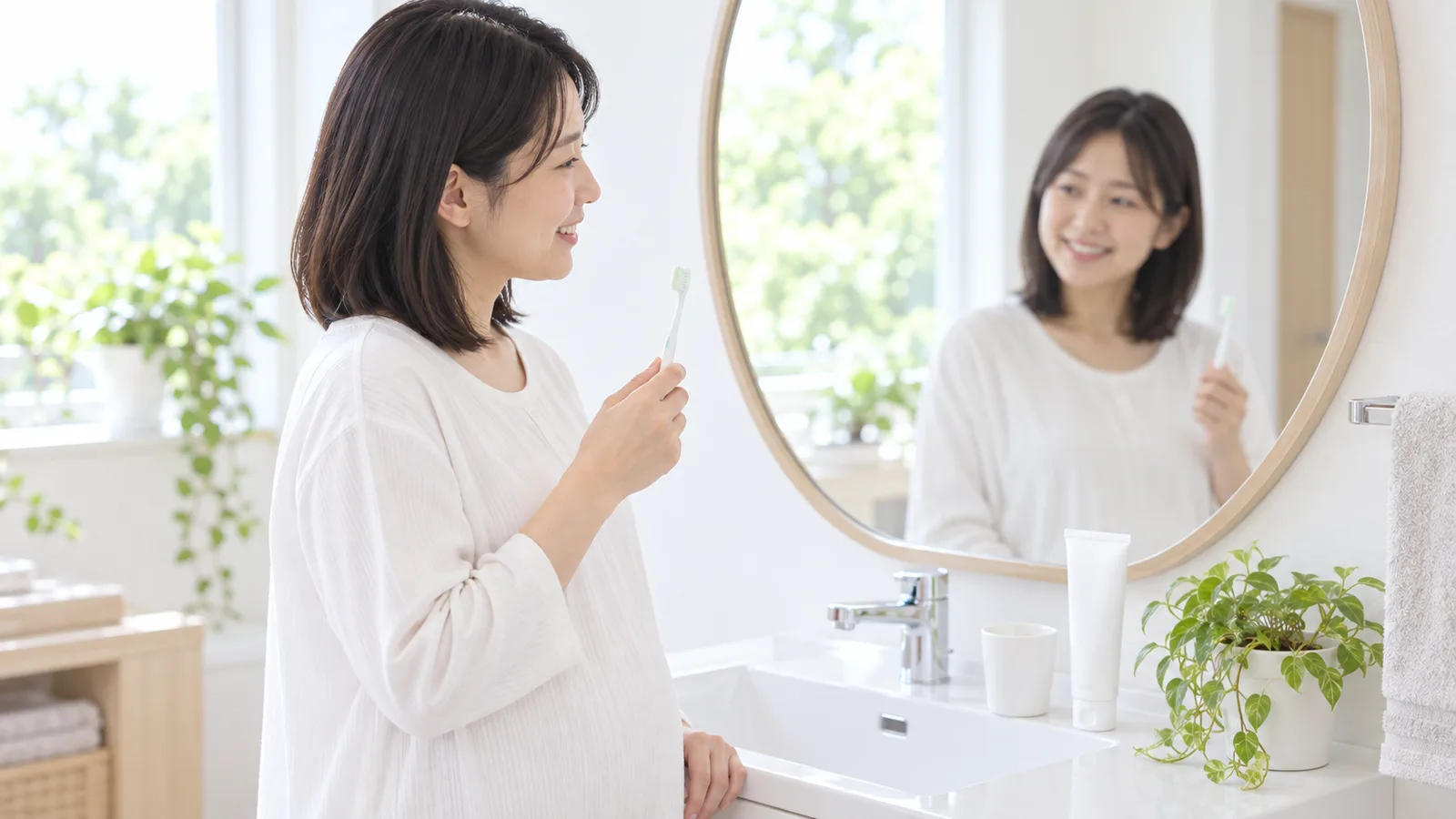 朝の洗面所で、妊婦さんがヘッドの小さな歯ブラシを手に、鏡の前に立っている