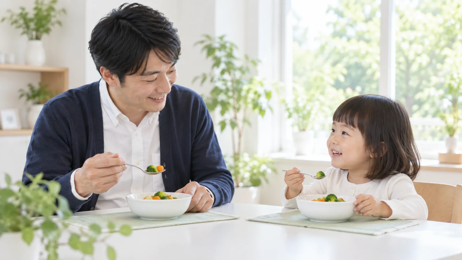 食卓で、父親と幼い女の子がそれぞれ自分のスプーンを持って向かい合っている