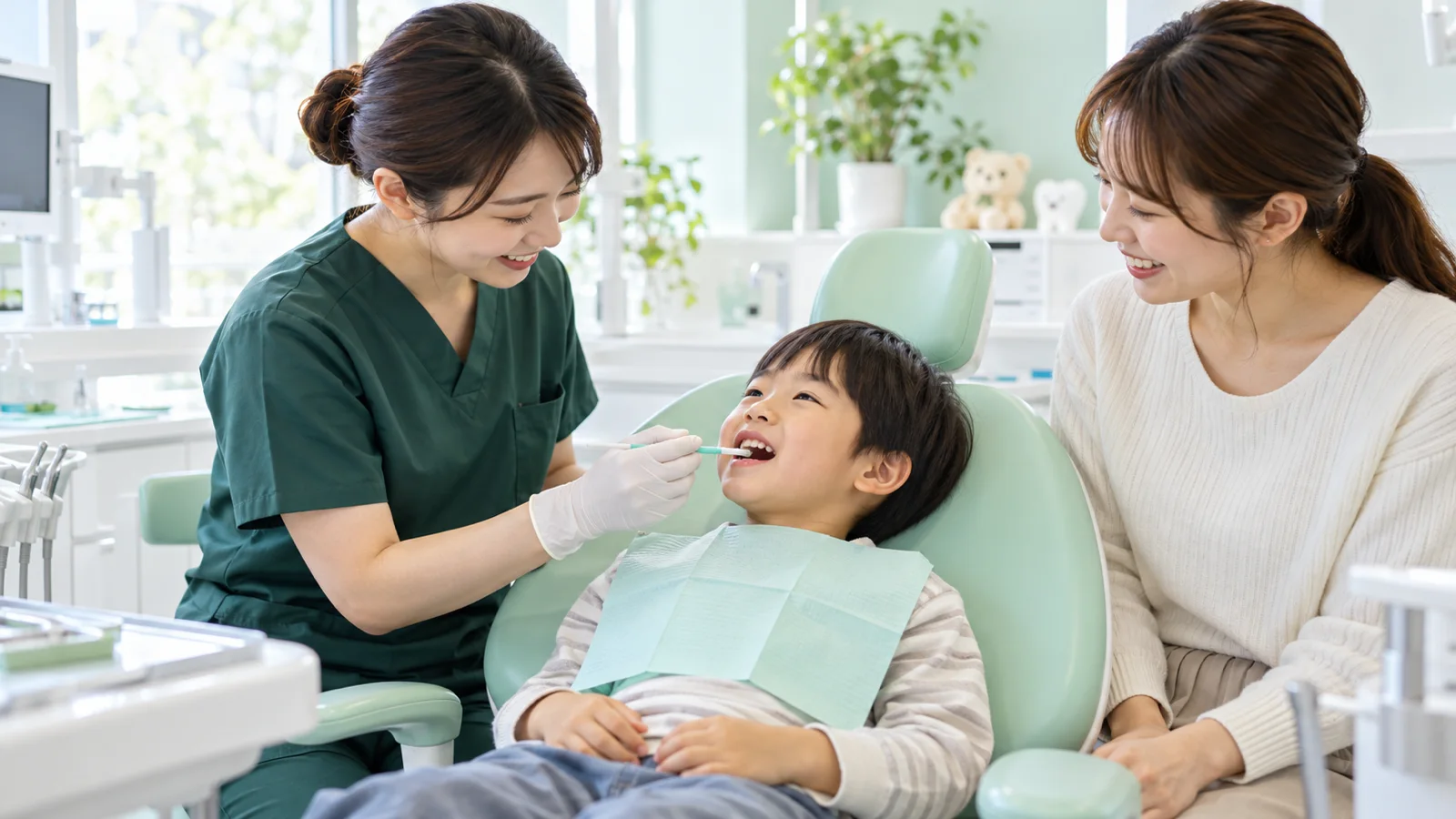 明るい診療室で、歯科衛生士がミントグリーンの診療台の男の子の歯に小さな筆でフッ素を塗り、母親がそばで見守っている