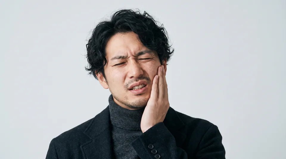 頬を手で押さえ、歯の痛みに顔をしかめる男性