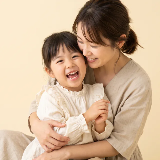 乳歯を見せて笑う女の子と、ほほえむ母親