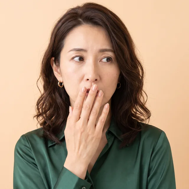 手で口元を覆い、息のにおいを気にする女性